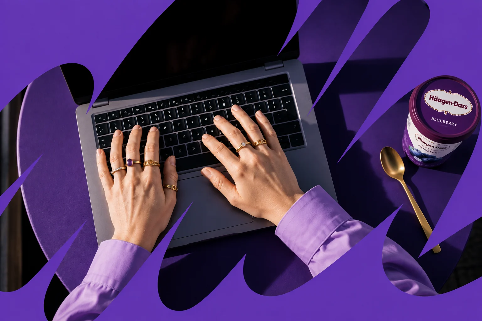 Hands working on a laptop in a purple creative workspace